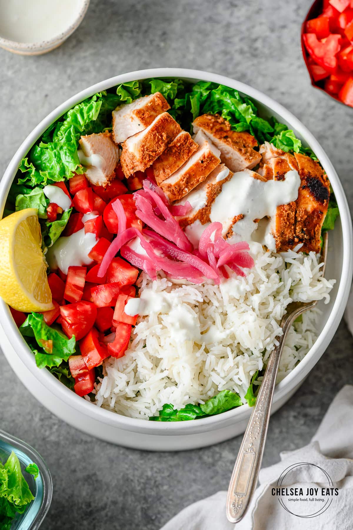 High protein chicken shawarama bowls with sliced shawarma chicken breast, green lettuce, rice, tomatoes, pickled onions, and garlic sauce in a white ceramic bowl.
