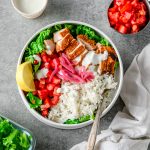 Gluten free chicken shawarama bowls with sliced shawarma chicken breast, green lettuce, rice, tomatoes, pickled onions, and garlic sauce in a white ceramic bowl.