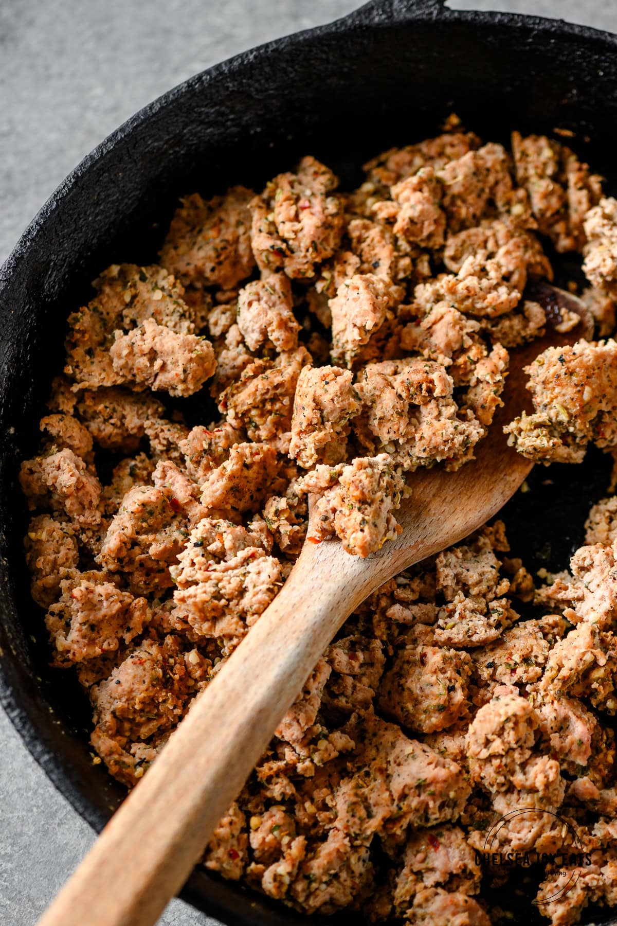 Wooden spoon stirring seasoned Italian ground turkey in a cast iron skillet.