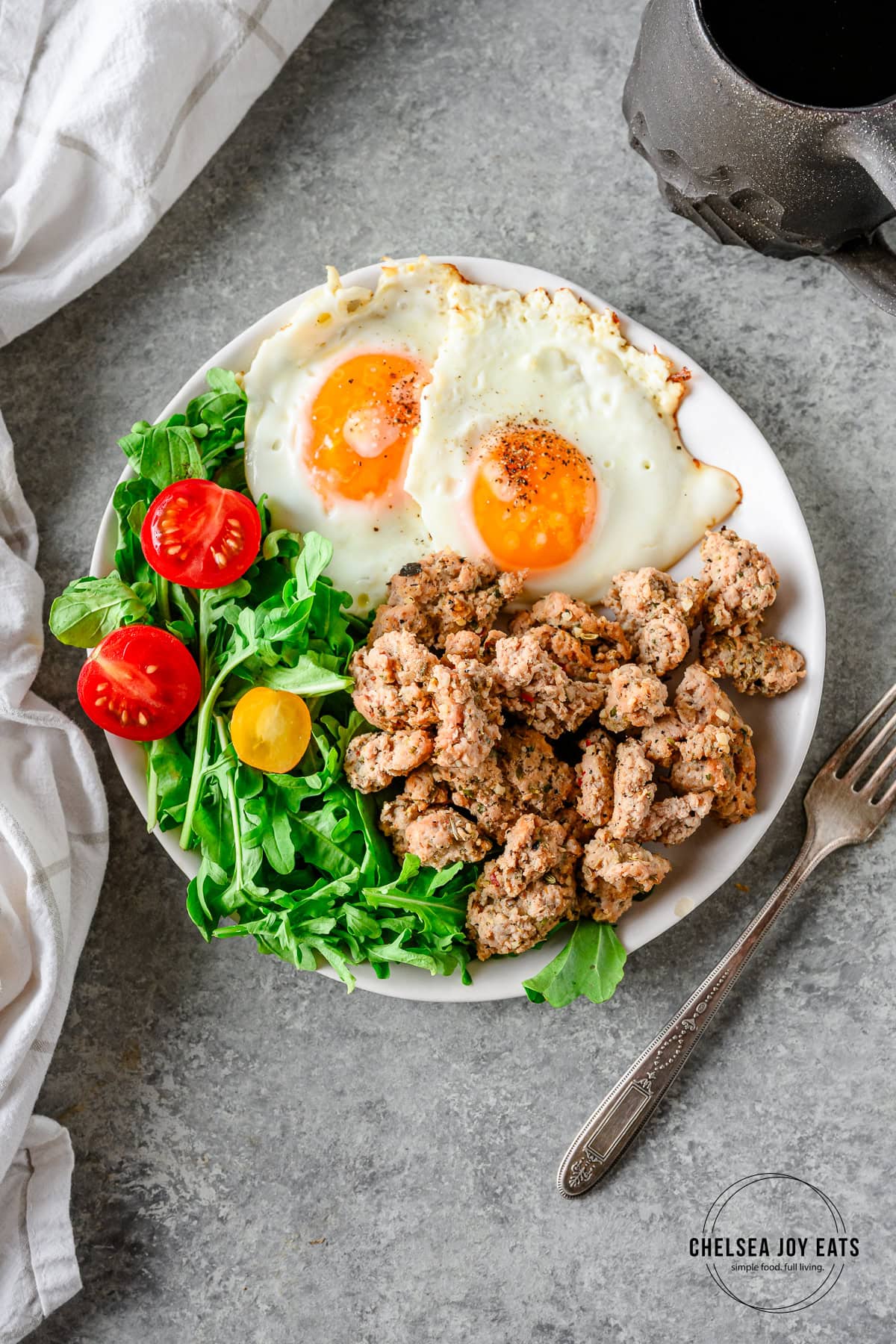 Cooked Italian Turkey Breakfast Sausage on a small white plate with an arugula salad and two fried eggs, with a fork besides.