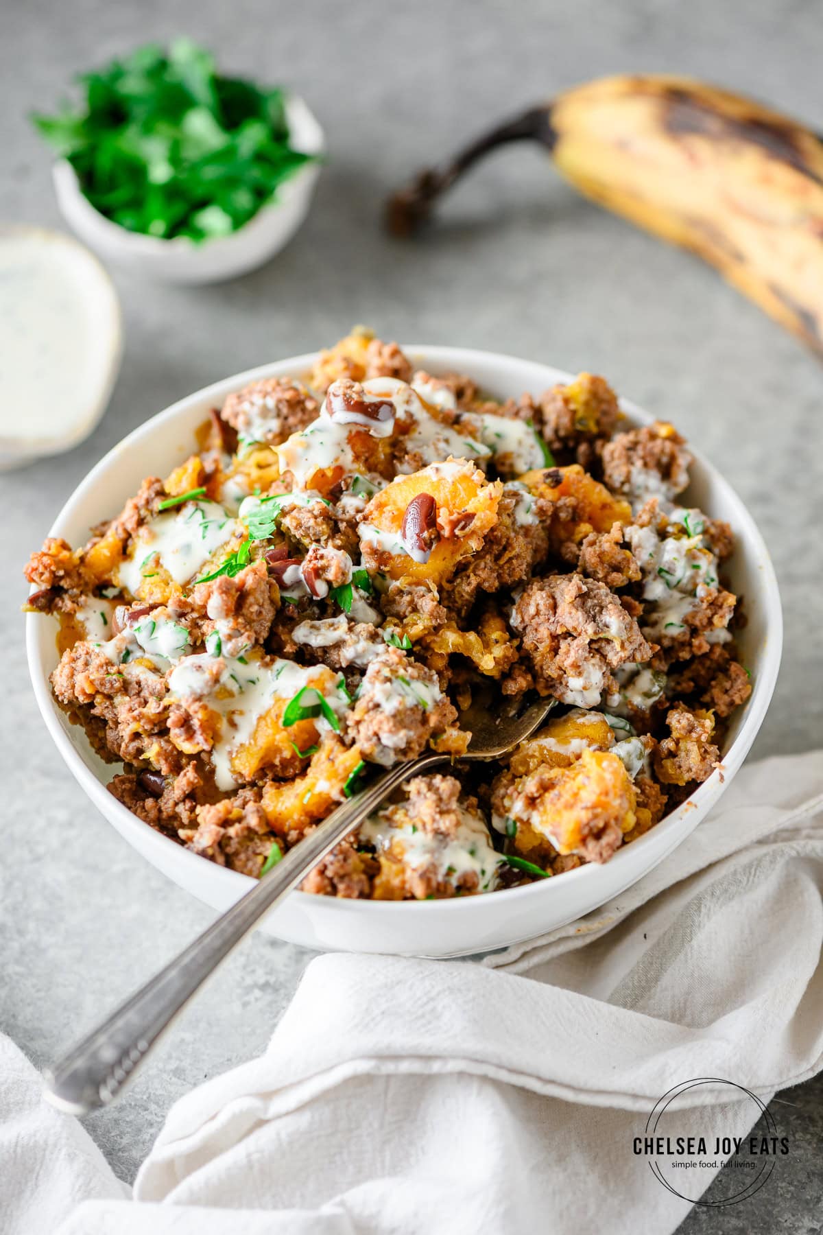 Plantain ground beef bowl drizzled with mayonnaise in a white bowl with a fork in the mixture.