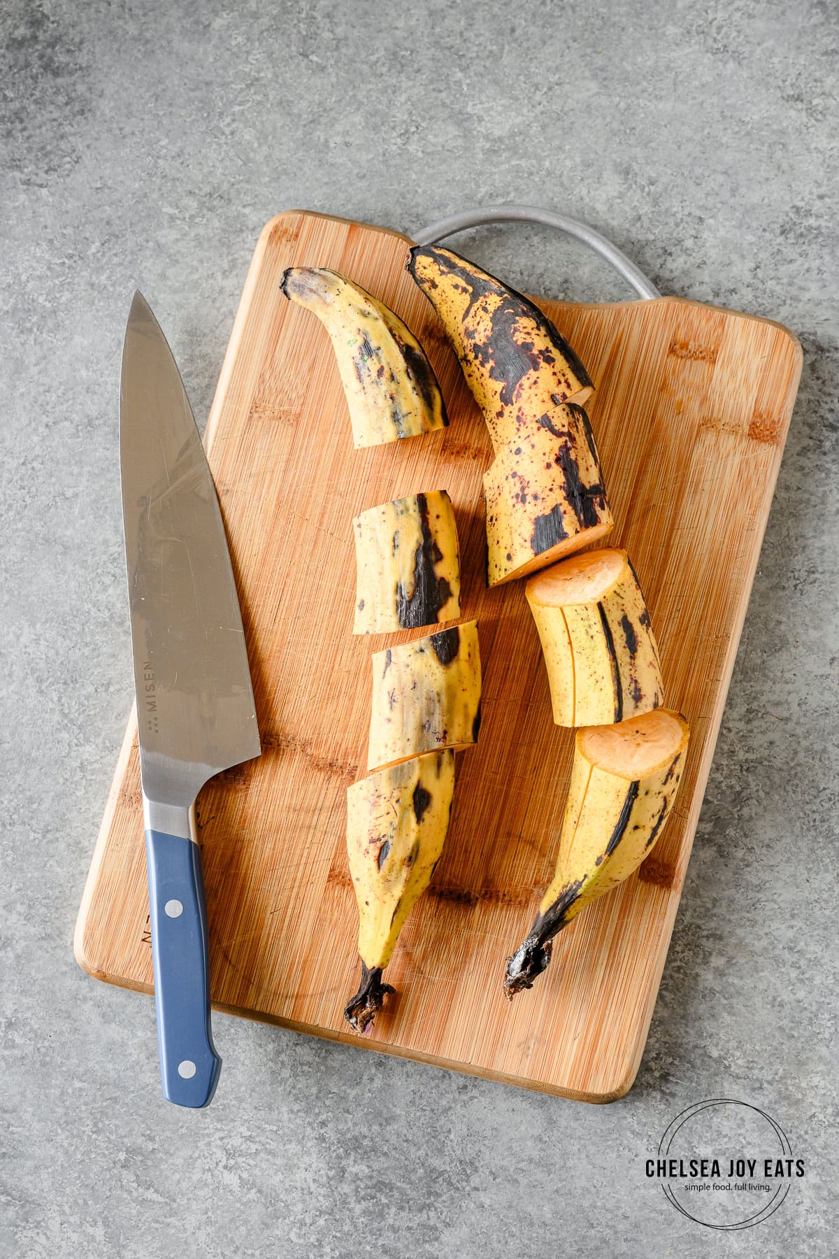 Two plantains sliced crosswise on a cutting board with a chef's knife alongside.