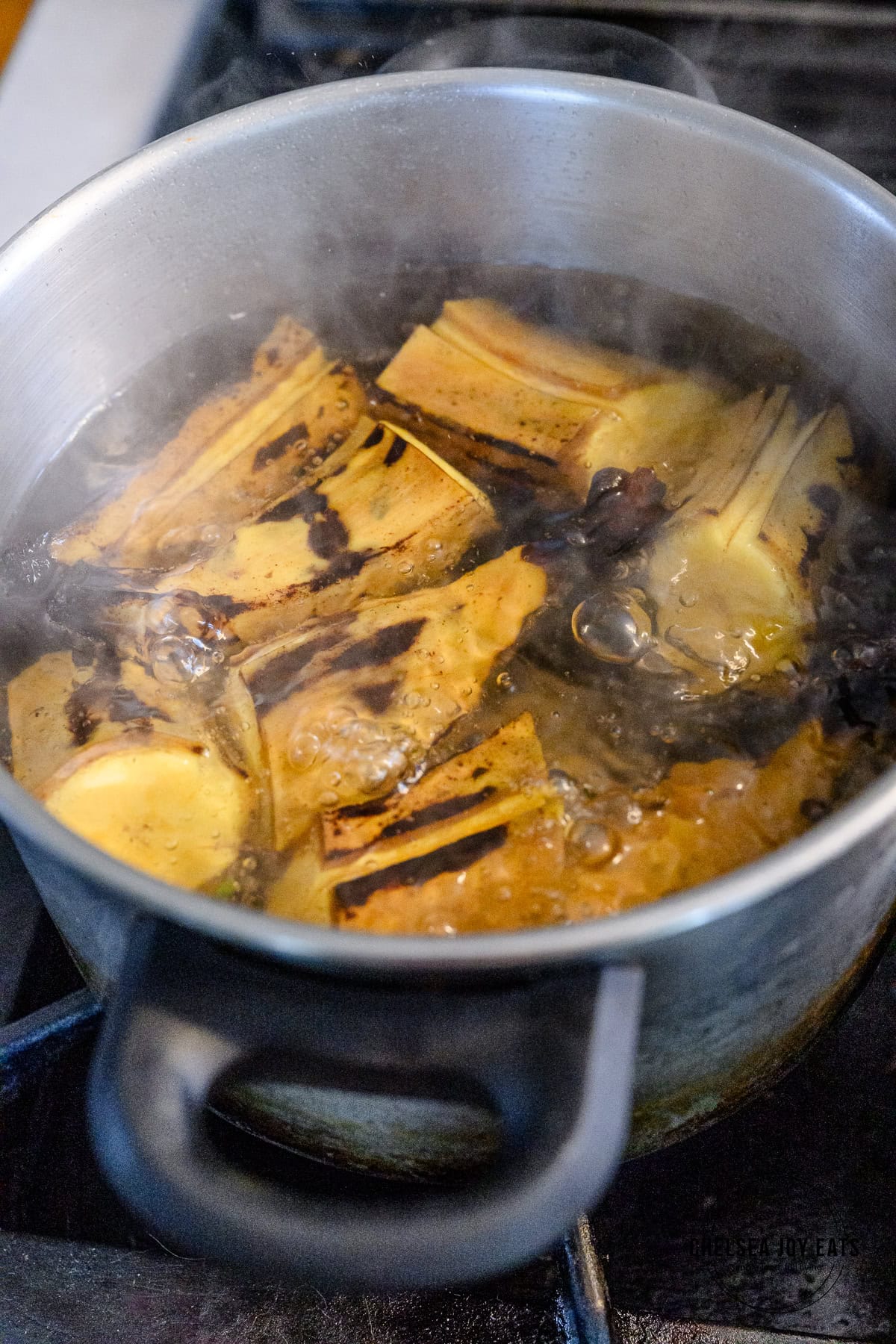Plantain sections boiling in a stainless steel pot on the stovetop.