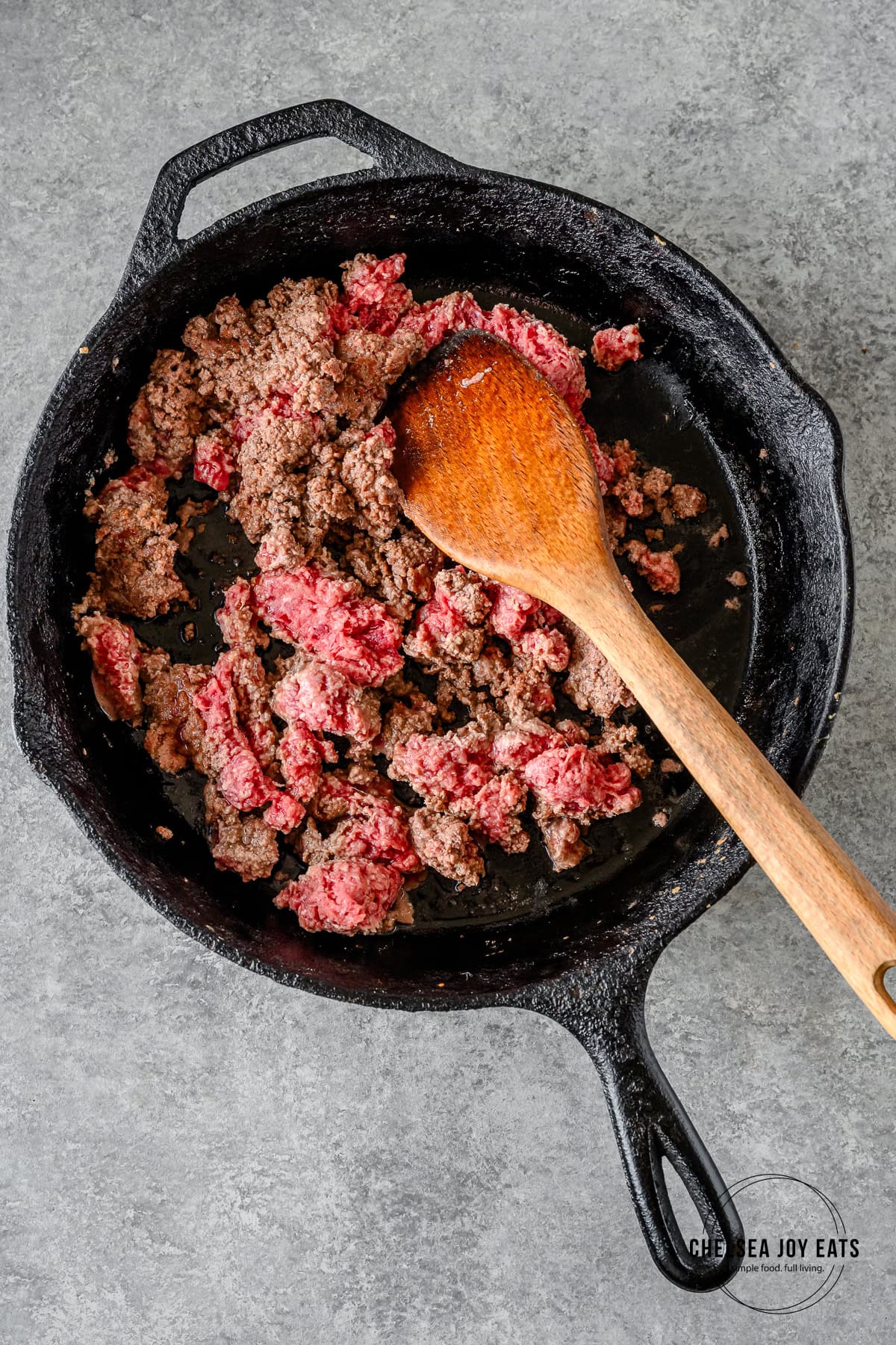 Ground beef browning in a cast iron skillet.