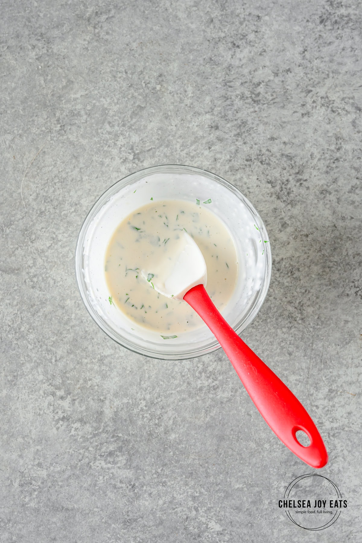 Parsley mayonnaise sauce stirred in a small glass bowl with a small spatula.