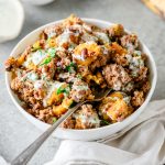 Ground beef bowl with plantains and olives topped with creamy sauce in a white bowl with a fork.