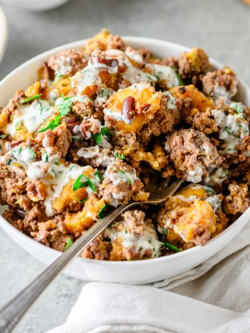 Ground beef bowl with plantains and olives topped with creamy sauce in a white bowl with a fork.
