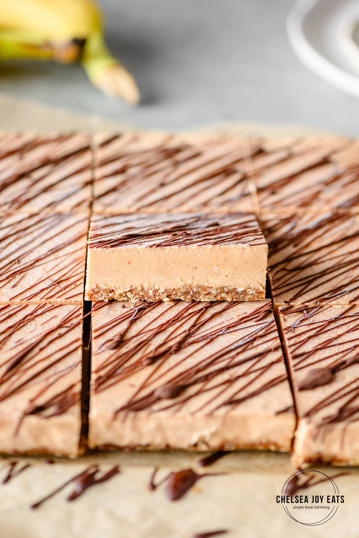 Rows of frozen protein no bake banana ice cream bars with one propped up to show its texture with plates and fresh bananas in the background.