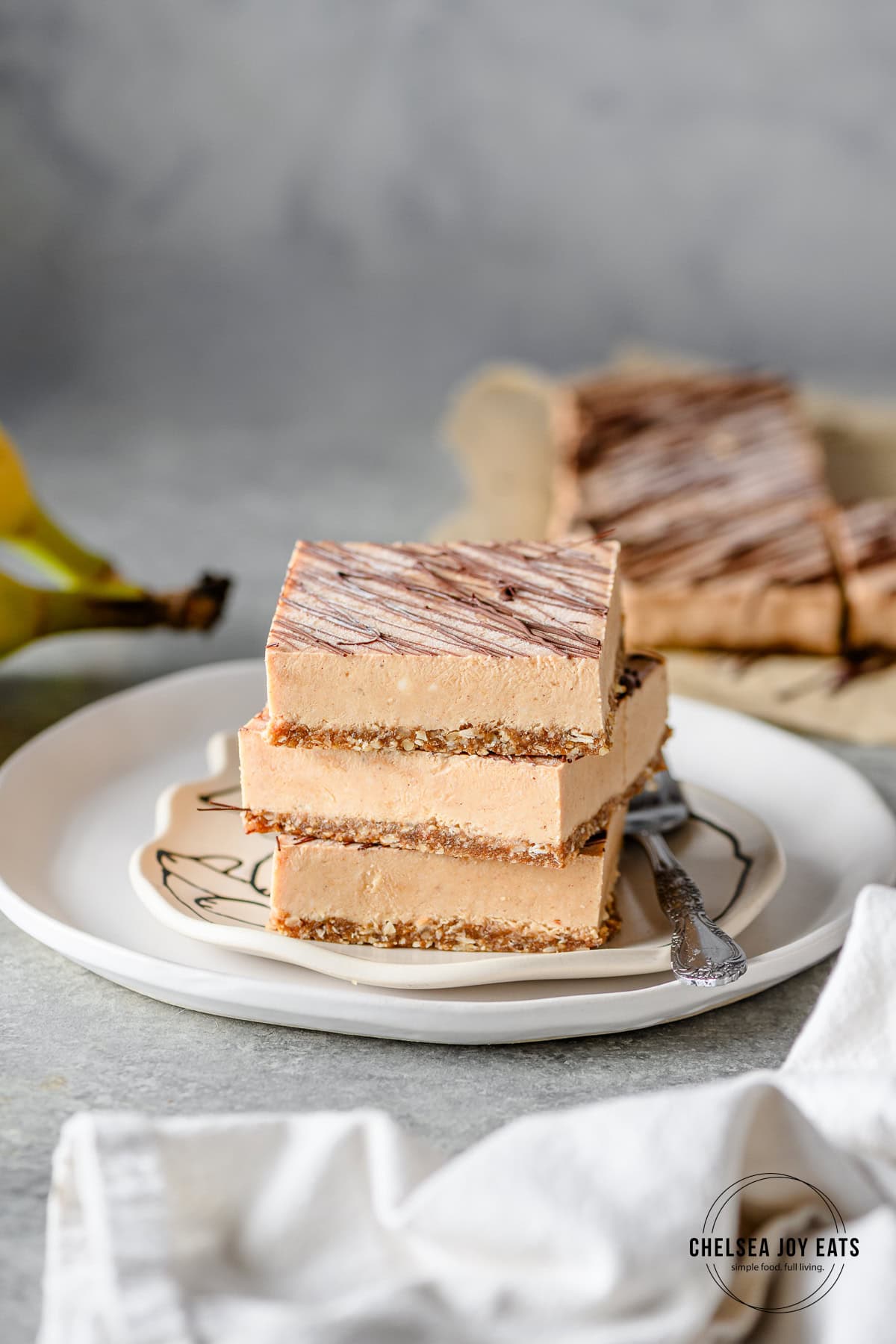 Three homemade no bake protein banana ice cream bars stacked on top of each other on a small plate with more bars in the background.