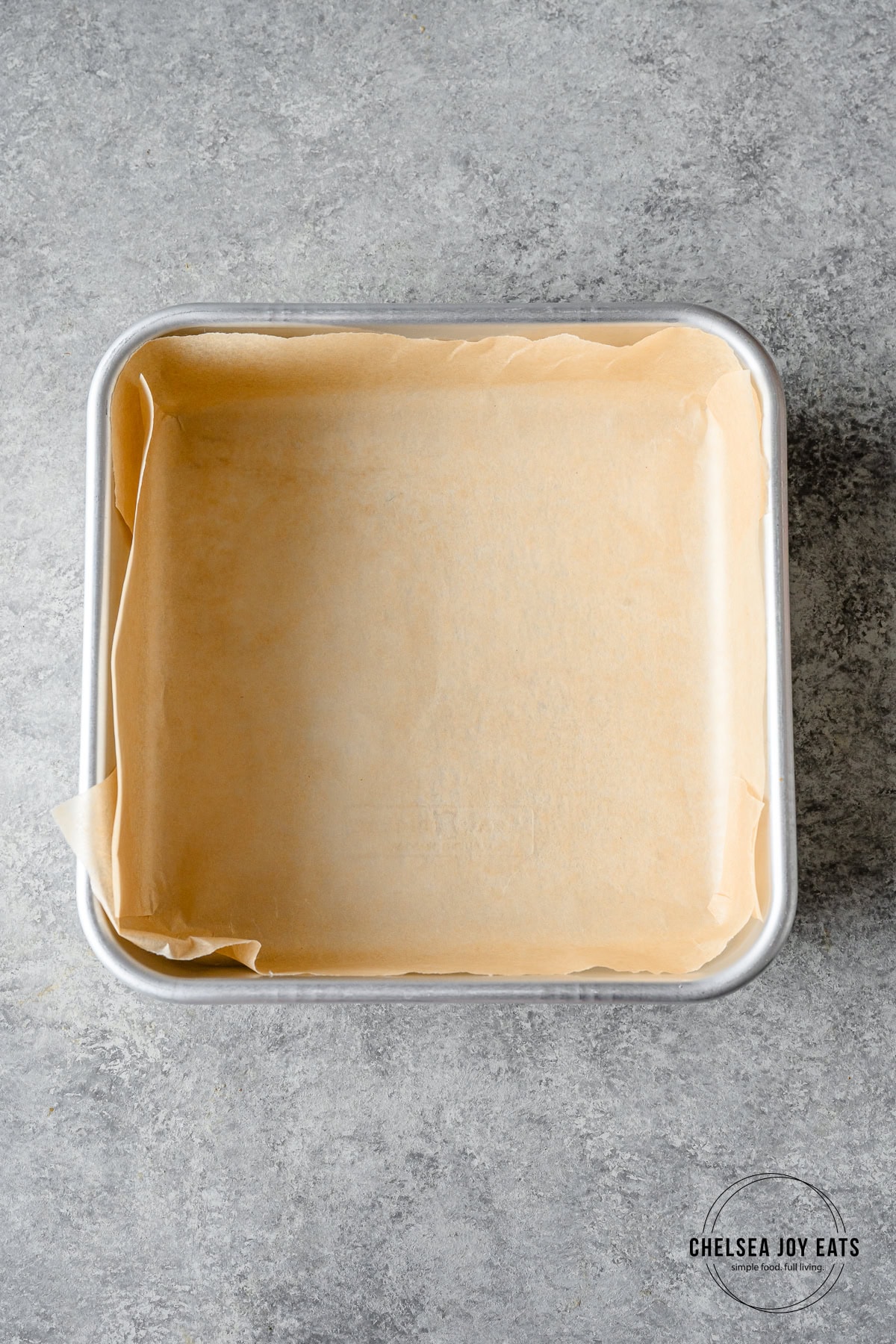 9x9 baking pan prepared with parchment paper lining the inside on a grey countertop.