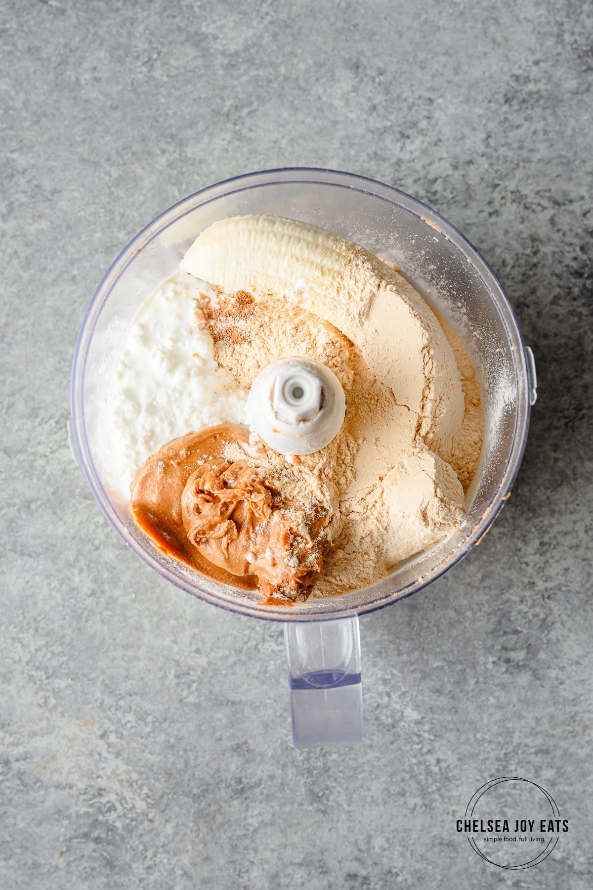 Cottage cheese, peanut butter, banana, and protein powder in the bowl of a food processor.