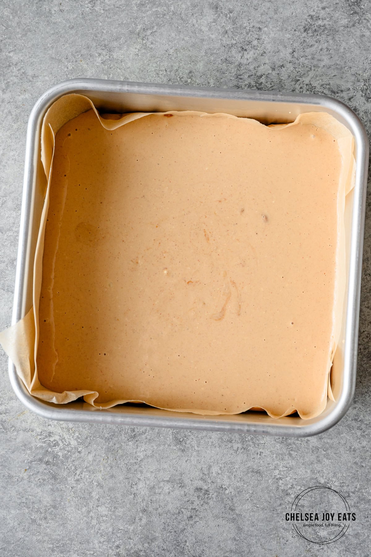 Smooth banana mixture in a baking pan lined with parchment paper on a grey countertop.