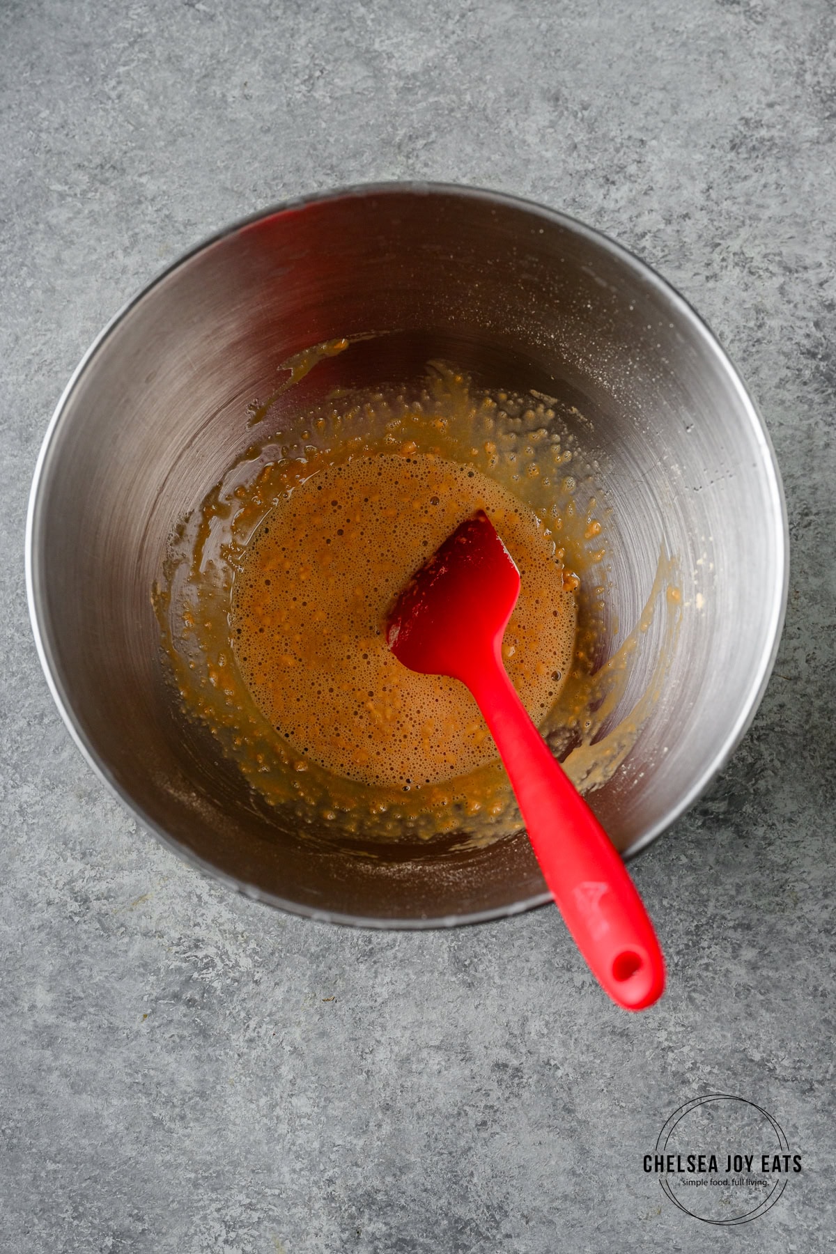 Protein powder and water mixed in the bowl of a stand mixer with a silicon spatula.