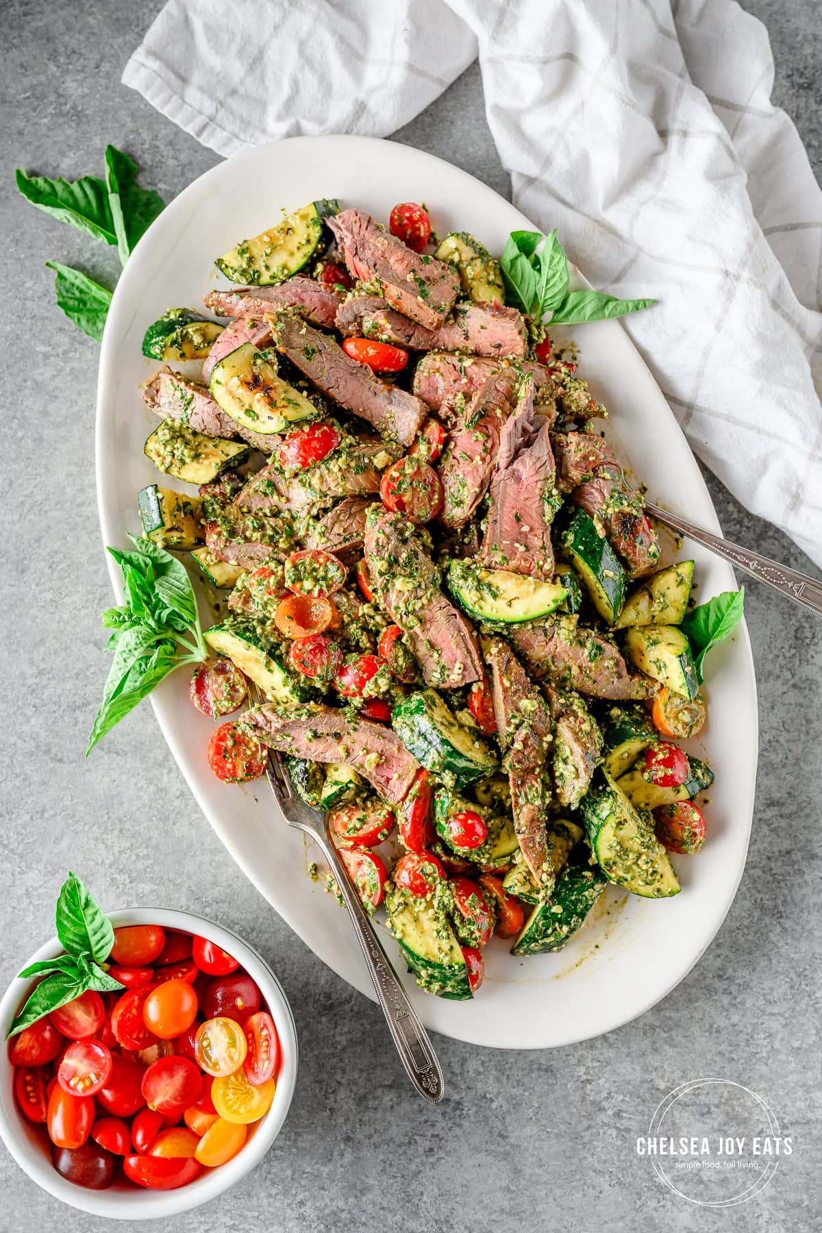 Assembled grilled steak salad with zucchini and pesto tossed together and served on a large white platter.