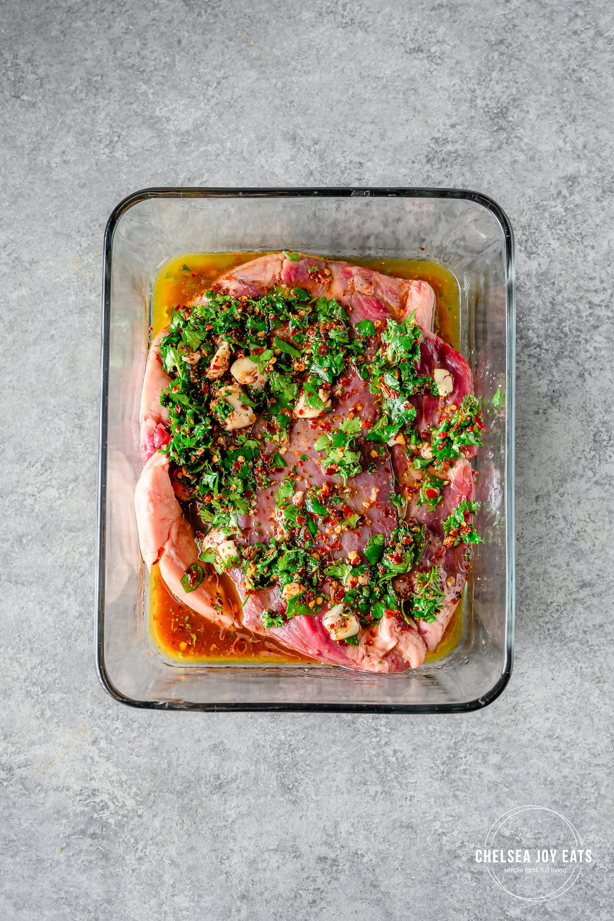 Flank steak with an herby marinade in a glass dish.