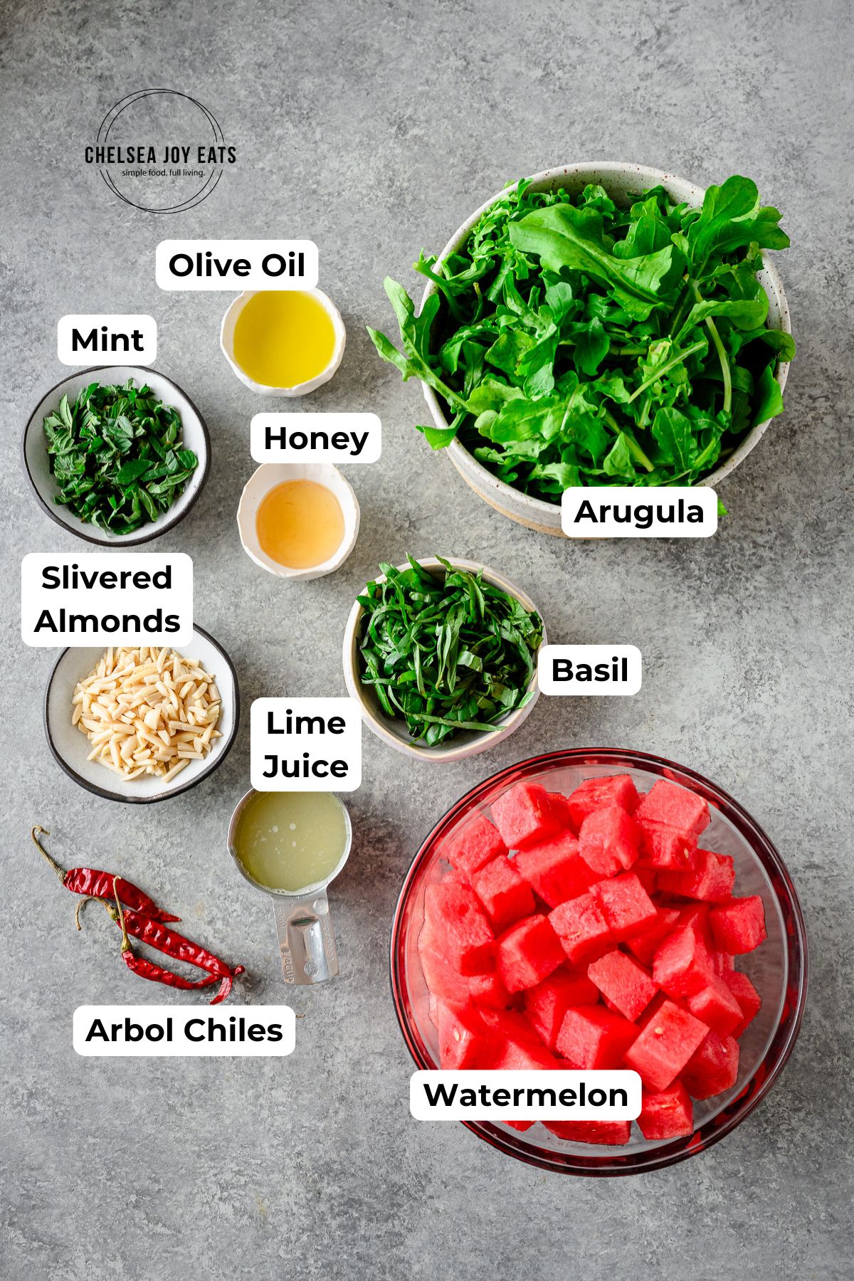 Ingredients for Watermelon and Arugula Salad in individual bowls with text labels for each ingredient.