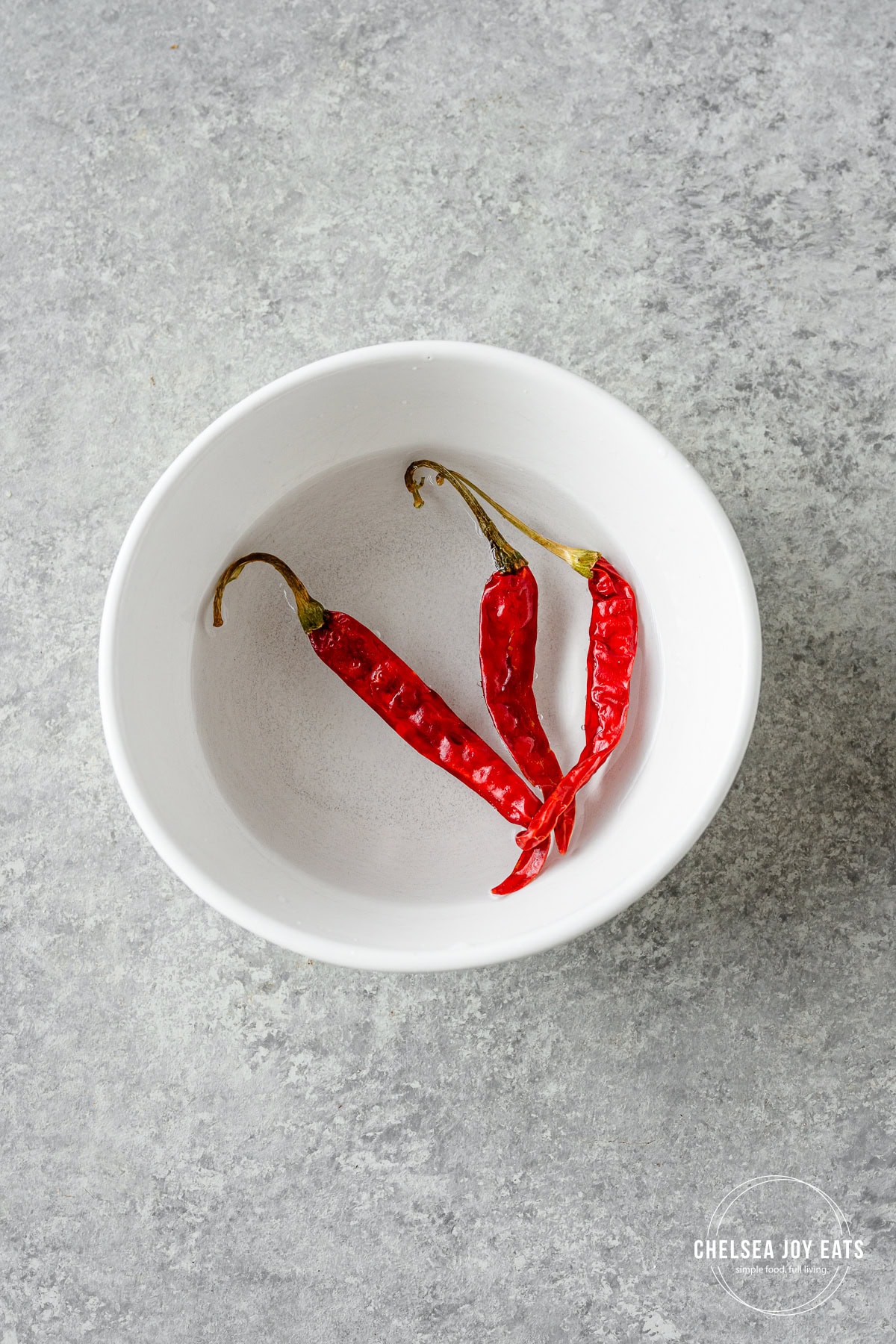 Dried arbol chiles softening in hot water in a small ceramic dish.