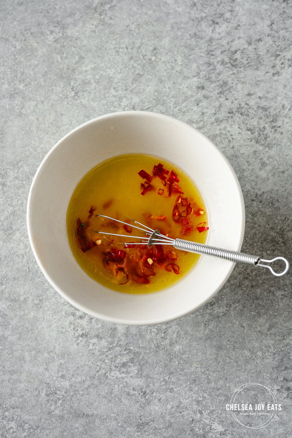 Chili honey lime dressing whisked with a small metal whisk in a ceramic dish.