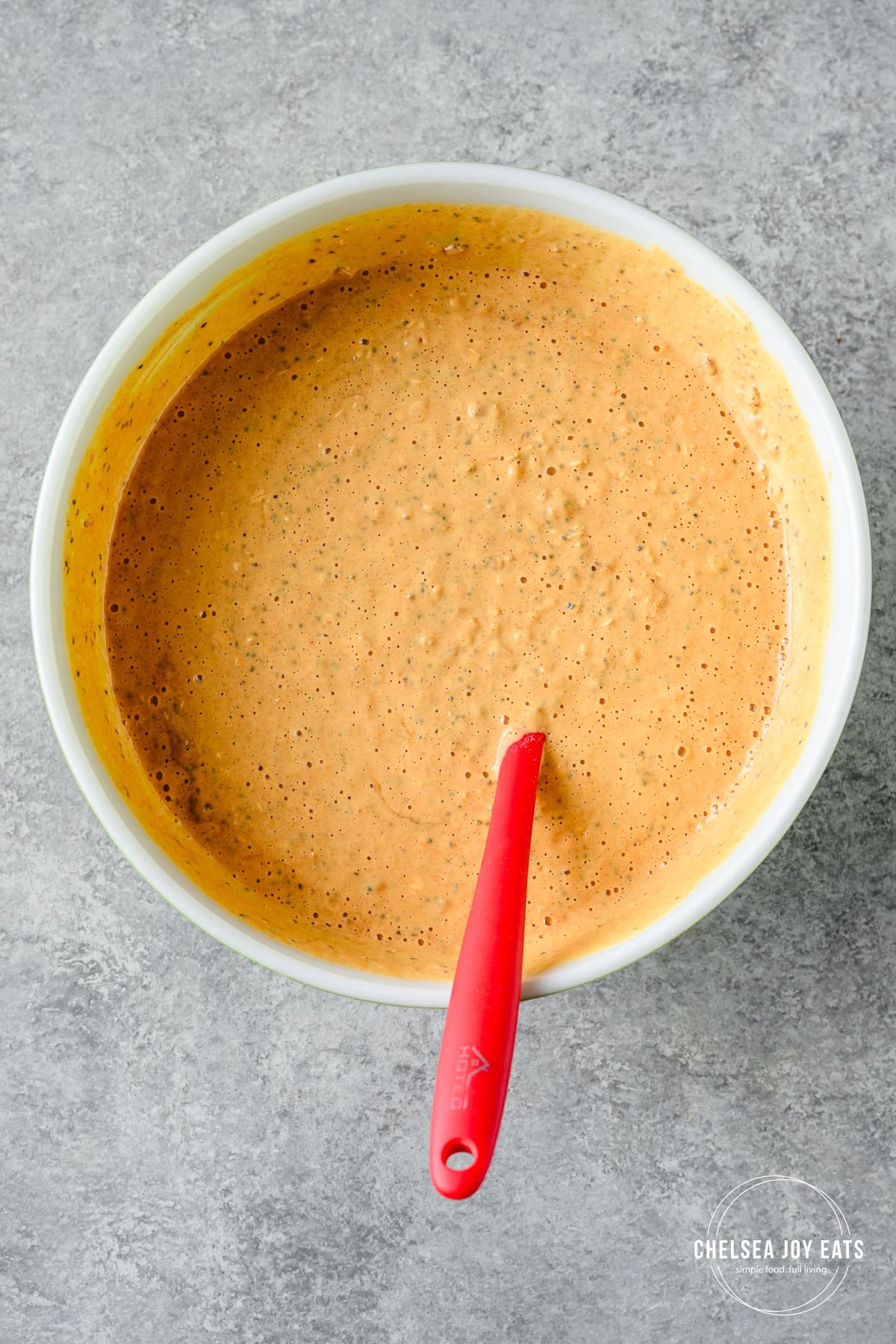 Oats, pumpkin, cottage cheese, and eggs stirred in a ceramic bowl with a silicon spatula.
