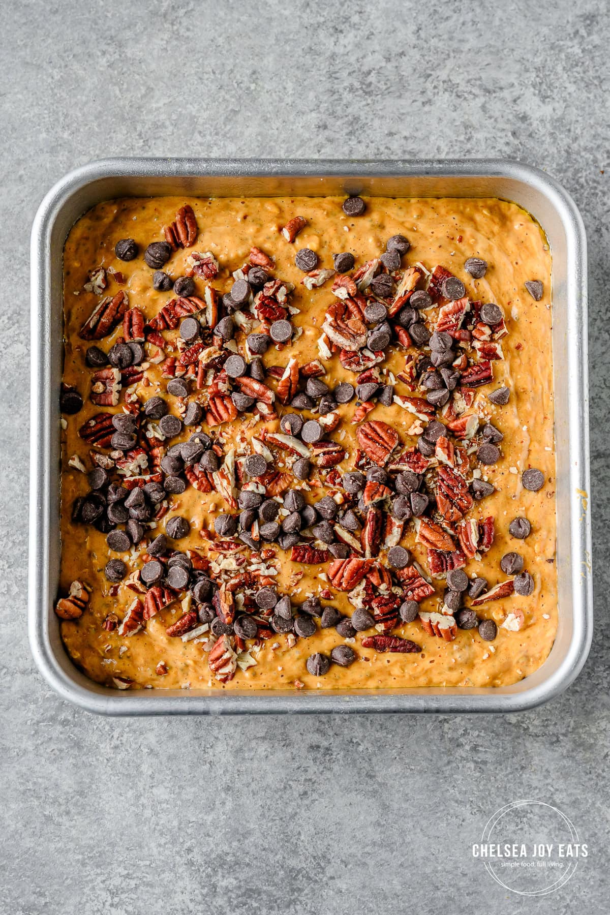 Uncooked pumpkin baked oatmeal in a baking pan topped with pecans and chocolate chips.