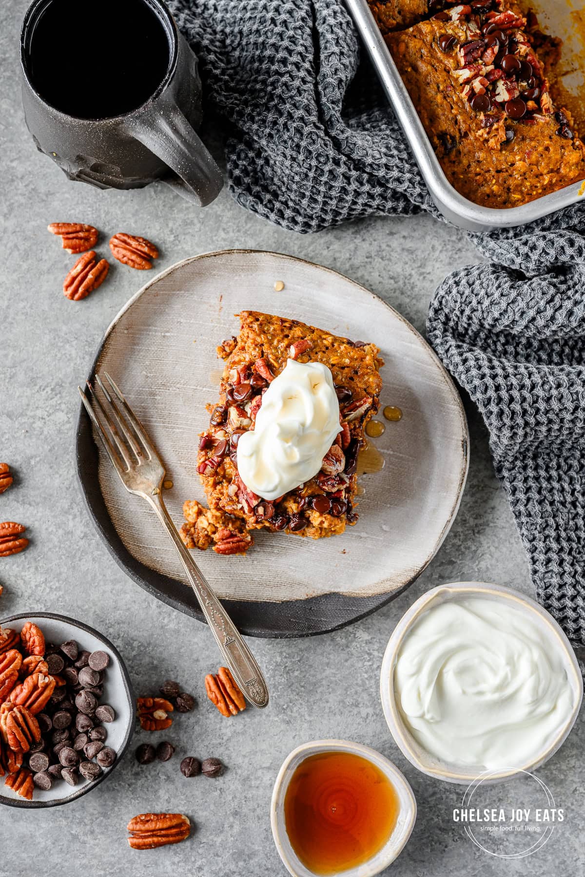 Serving of gluten free baked pumpkin oatmeal topped with Greek yogurt and drizzled with maple syrup on a ceramic plate with extra toppings and a fork alongside.