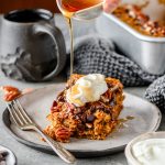 Serving of gluten free pumpkin baked oatmeal topped with Greek yogurt and drizzled with maple syrup on a ceramic plate with a cup of coffee in the background.