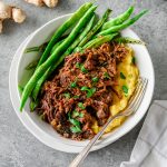 Shredded braised chuck roast served over polenta with sautéed green beans with a fork alongside.