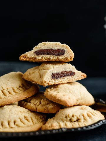 Stack of gluten free date-filled cookies on a small tray, with one cookie sliced in half to show the date filling.