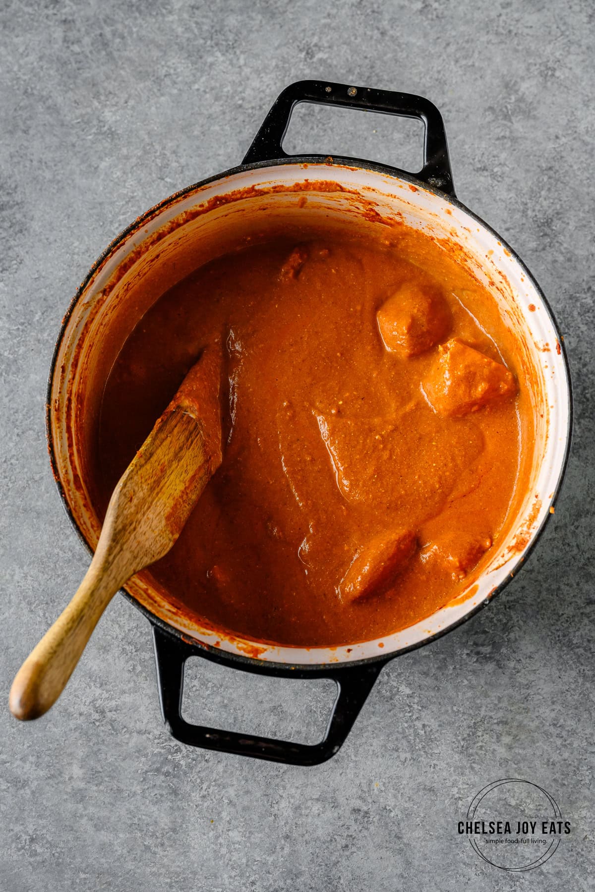 Tikka masala with chicken breast in a Dutch oven being stirred with a wooden spatula.