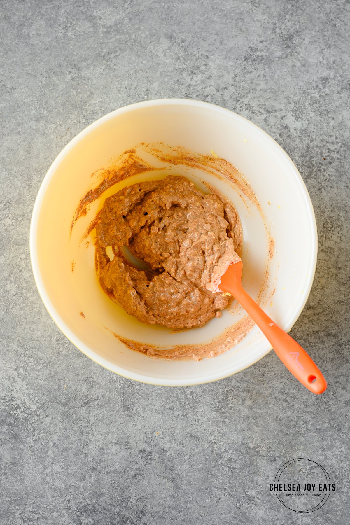 Marinade for tikka masala chicken stirred in a ceramic bowl with a silicon spatula.