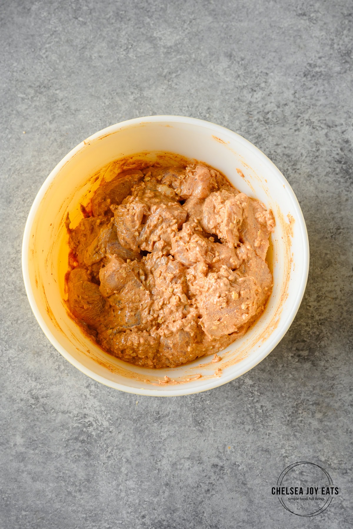 Chicken pieces covered in tikka masala marinade in a ceramic bowl on a grey background.