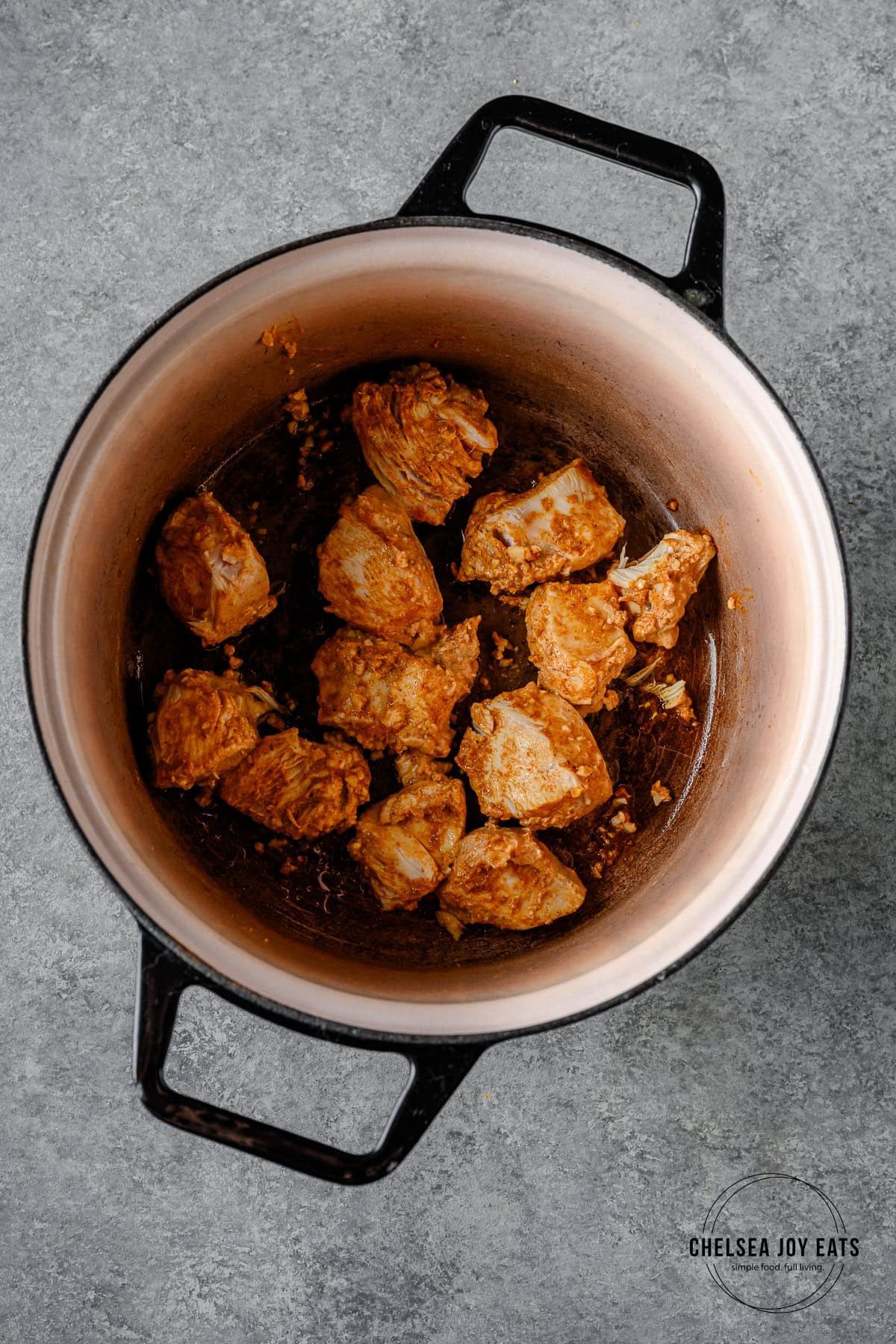 Marinated chicken pieces searing in a Dutch oven.