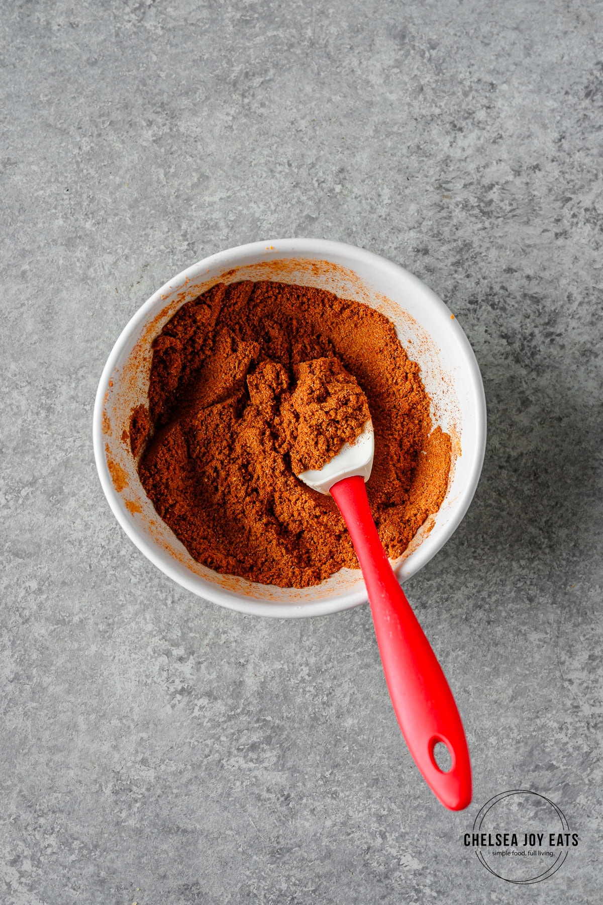 Curry spices for tikka masala stirred in a small ceramic bowl with a silicon spatula.