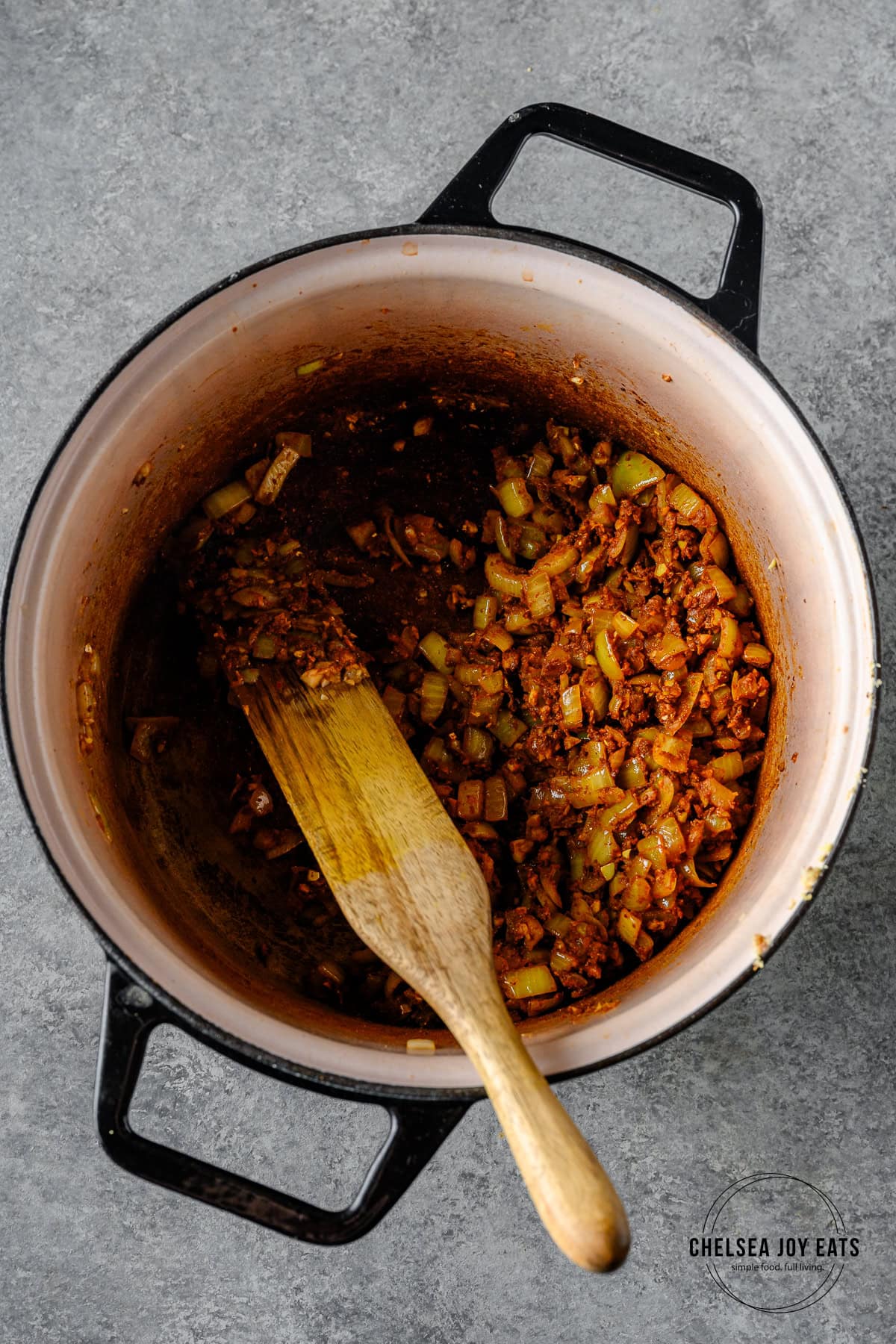 Onions, garlic, ginger, and curry spices sautéing in a Dutch oven, with a wooden spatula stirring.